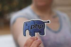 Eine Hand hält einen Aufkleber in Form eines blauen Elefanten mit der Aufschrift "php", der das Logo der Programmiersprache PHP darstellt.