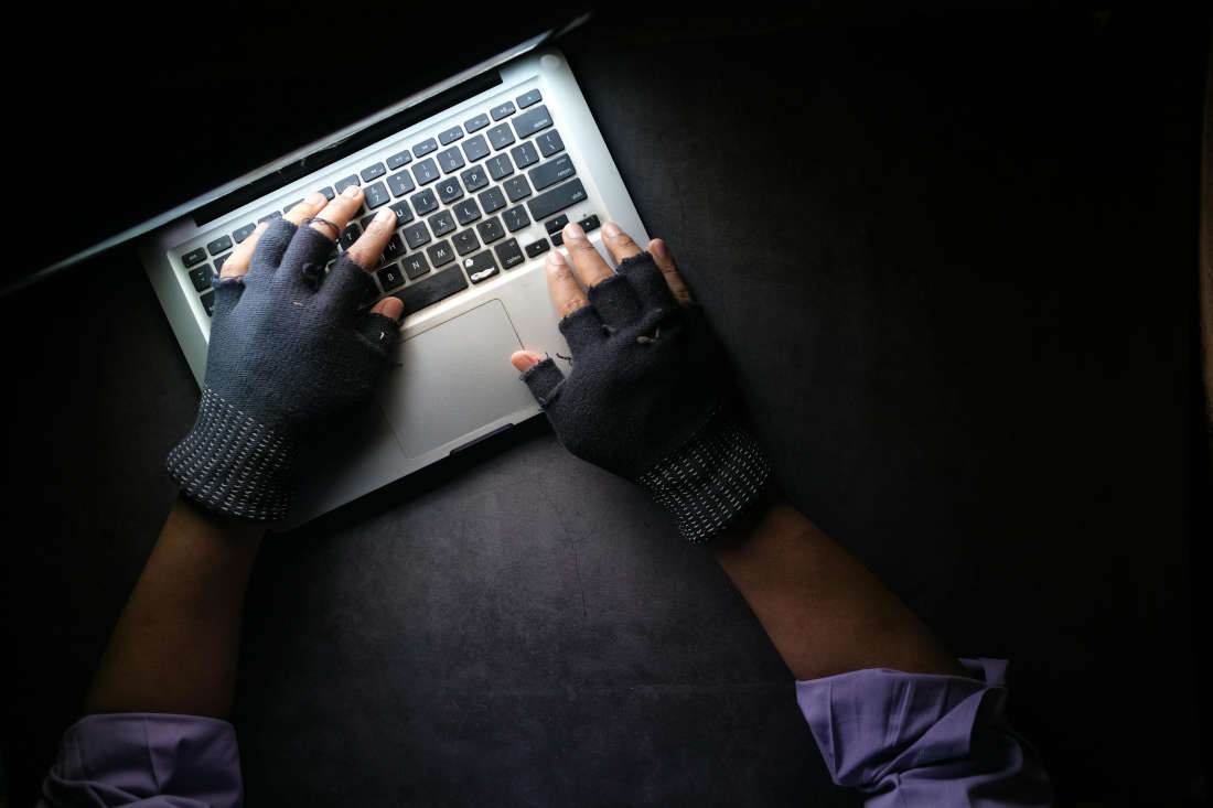 Eine Person mit Handschuhen tippt in dunkler Umgebung auf einer Laptop-Tastatur.